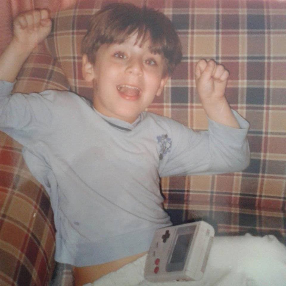 Young JV cheering on a couch with a gameboy on his lap